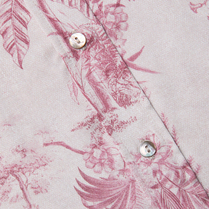 Close-up of a light pink Dani Silk Blouse with a red jungle toile print, highlighted by two iridescent buttons and intricate leaf and flower details.