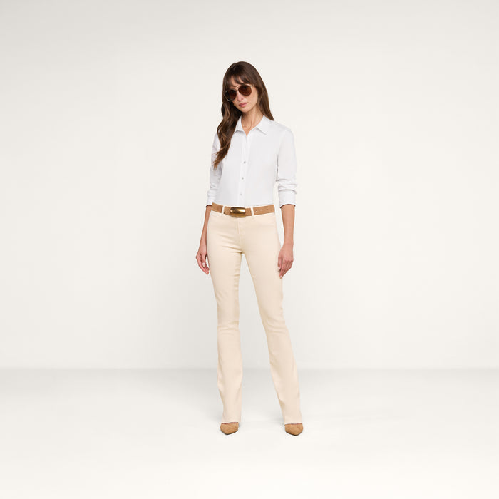 A woman wearing sunglasses, the Daniella Cotton-Blend Blouse with three-quarter sleeves, beige pants with a brown belt, and beige heels stands against a plain white background.