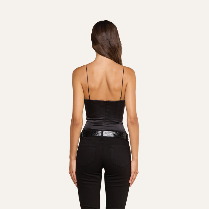 A woman with long brown hair, seen from the back, wears the Dara Stretch-Satin Bodysuit with adjustable straps, paired with black jeans and a black belt against a plain light background.