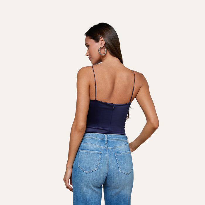 A woman with long brown hair, wearing hoop earrings, blue jeans, and the Dara Stretch-Satin Bodysuit with adjustable navy straps, is shown from the back against a plain light background.