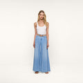 A woman stands facing forward, wearing a white tank top and the Dariela Wide-Leg Jean in ultra wide leg, light blue featherweight denim, styled with a tan belt and sandals, against a plain white background.