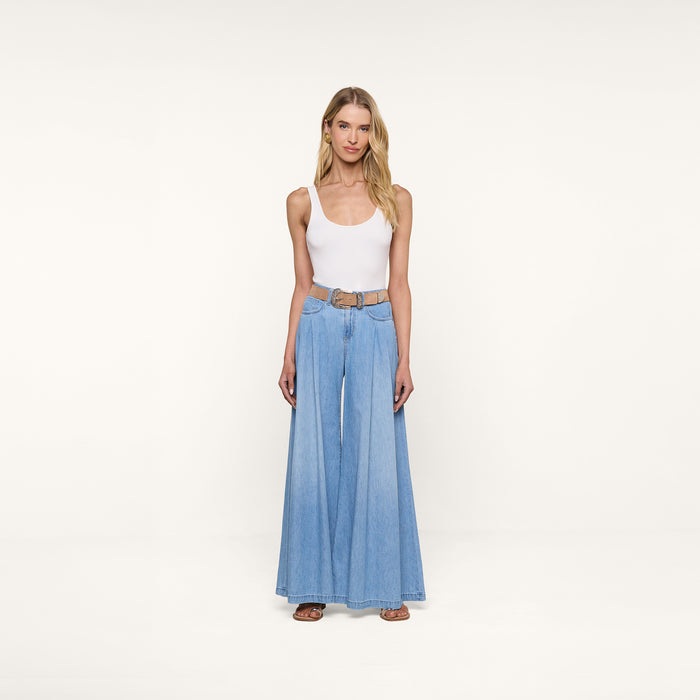 A woman stands facing forward, wearing a white tank top and the Dariela Wide-Leg Jean in ultra wide leg, light blue featherweight denim, styled with a tan belt and sandals, against a plain white background.