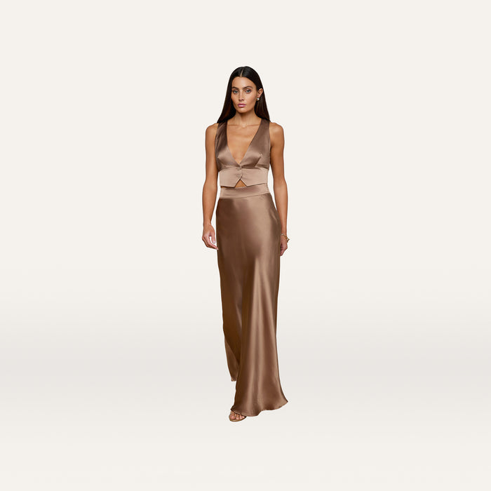 A woman in the Devony Silk Vest, a bronze satin tailored sleeveless crop top, paired with a long skirt, stands against a plain white background.
