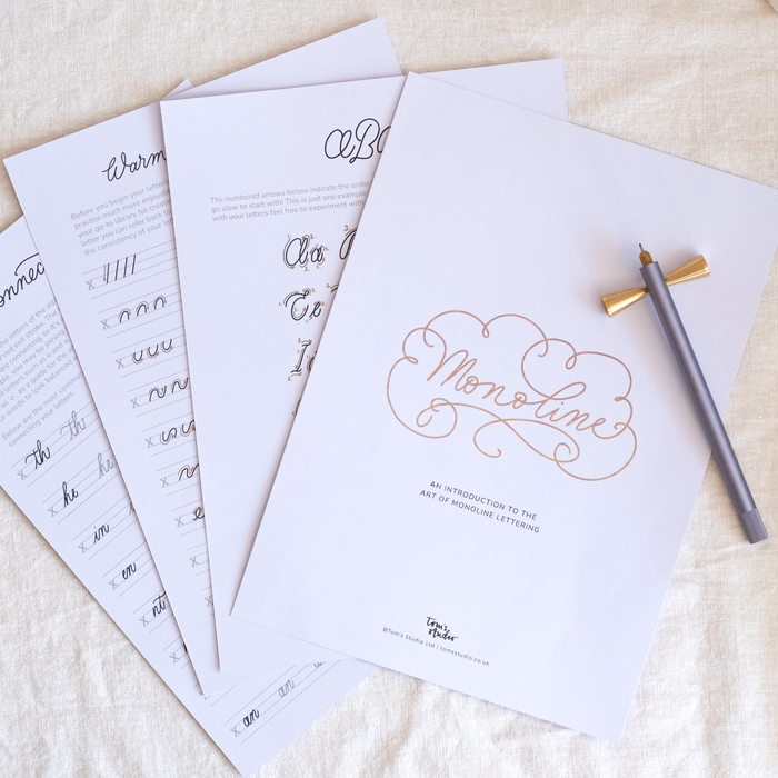 Flat-lay of several pages from the Monoline Lettering Guide, including the cover page, warm-up strokes, alphabet guides, and connecting letters. A lilac-coloured Lumos pen with brass butterfly pen rest is placed on top.