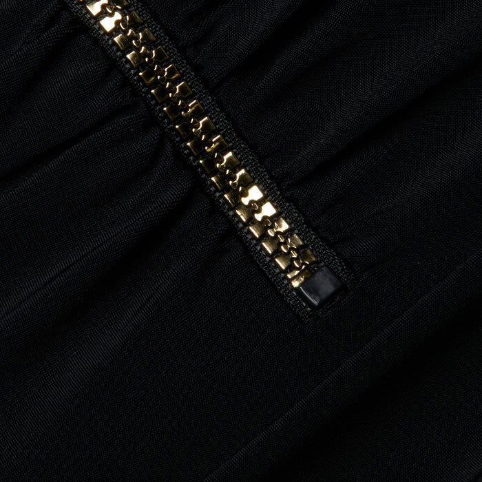 Close-up of the Dorrie Plunge One-Piece Swimsuit, featuring sleek black fabric with gathered stitching and a gold metallic zipper running diagonally across the design.