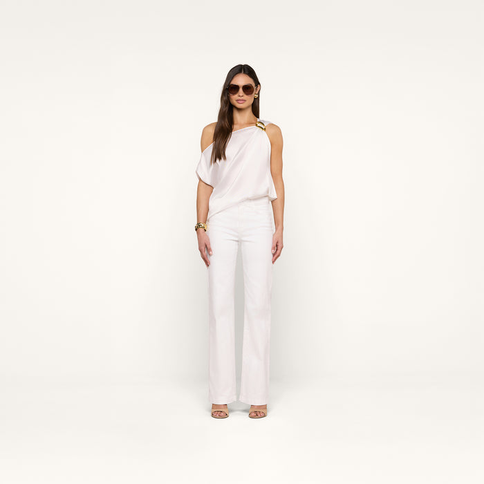 A woman poses against a beige background wearing the Driselle Scarf Top—white satin with a gold buckle—styled with wide-leg pants, sunglasses, gold jewelry, and heeled sandals.