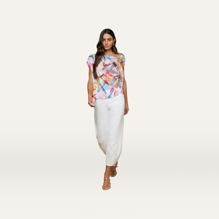 Wearing the Driselle Scarf Top with its colorful abstract pattern, paired with white loose pants and strappy sandals, she stands against a plain light background—perfect vacation wear.