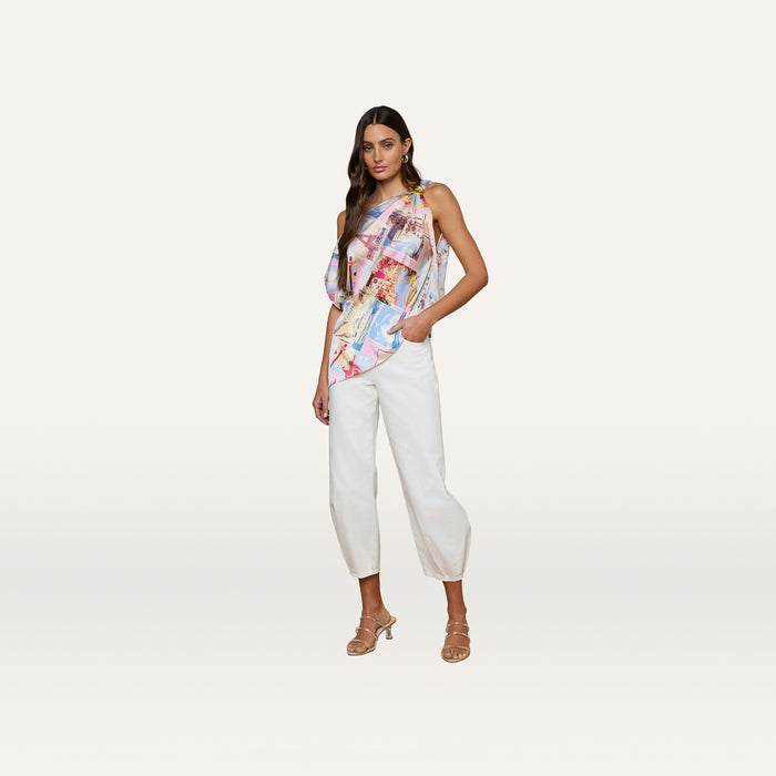 A woman stands against a plain background, wearing the Driselle Scarf Top paired with white cropped pants and beige heeled sandals, one hand in her pocket and the other by her side—an effortless look perfect for vacation wear.