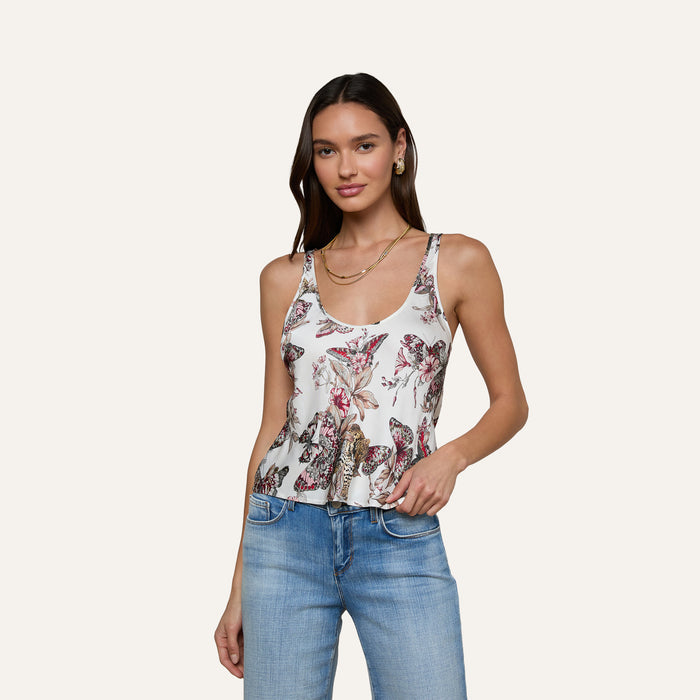 A woman models the Eddie Tank—a white sleeveless top featuring a vibrant floral print and a scoop neckline—paired with blue jeans against a plain light background.