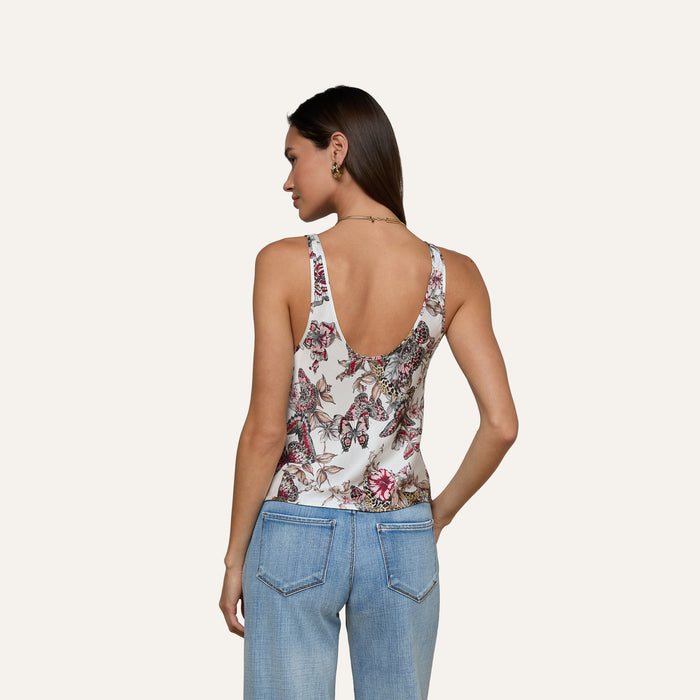 A woman with long brown hair, wearing the Eddie Tank—featuring a vibrant floral print—and light blue jeans, stands with her back to the camera against a plain light background.