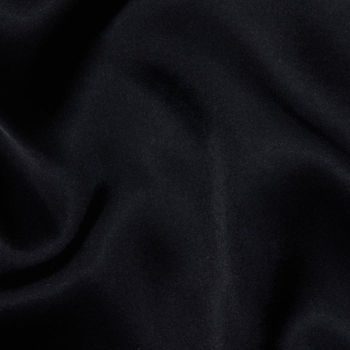 The Eddie Tank features soft, black fabric with a smooth texture and gentle, flowing folds that create subtle highlights and shadows across the material, enhanced by its flattering drape.