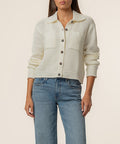 Cream knit sweater jacket with collar, button front, textured weave, and ruched sleeves worn with blue jeans.