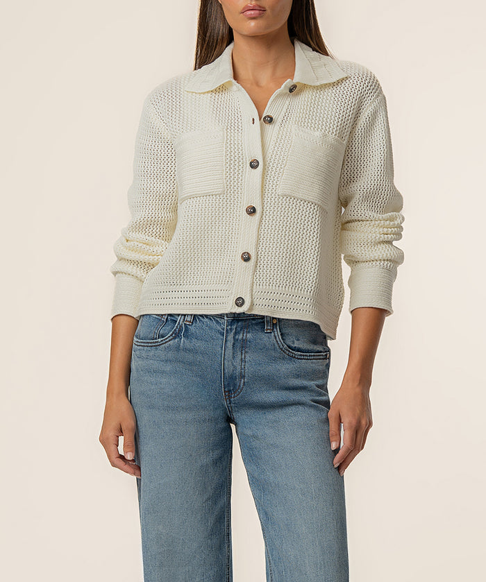 Cream knit sweater jacket with collar, button front, textured weave, and ruched sleeves worn with blue jeans.