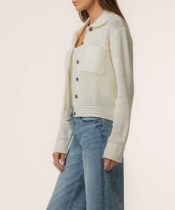 Cream knit cardigan jacket with textured pattern, button front, and ribbed cuffs worn over white top and blue jeans.