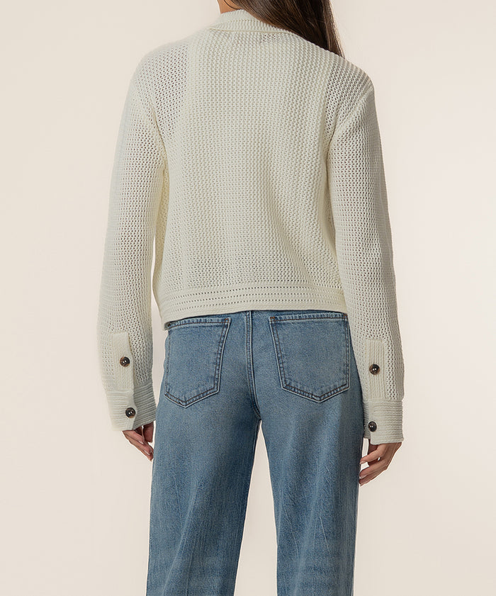 Cream knit sweater jacket with button cuffs, shown from back worn with blue jeans.