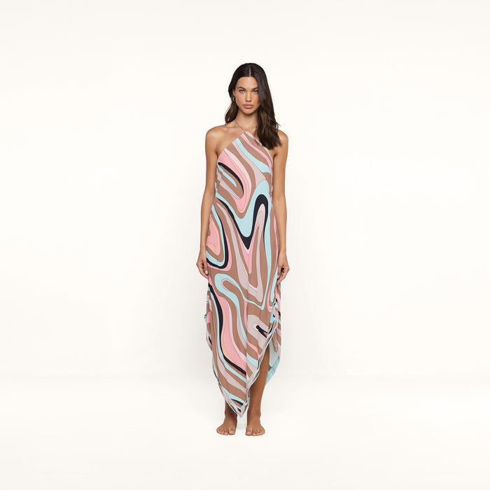 A woman stands barefoot against a white background, wearing the Elise Cover-Up Dress—a halter midi dress crafted from water-safe crepe and showcasing an abstract swirl print in pink, beige, blue, and black tones.