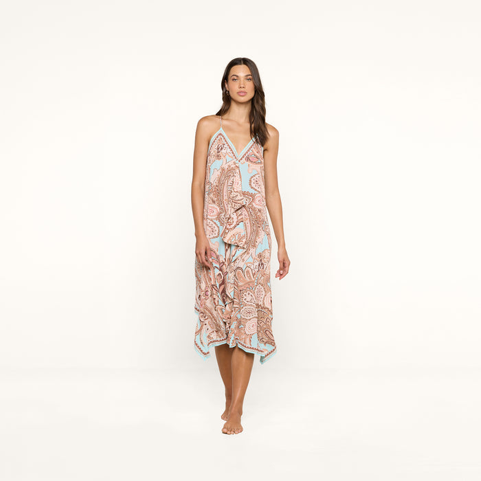 A woman stands barefoot against a white background, wearing the Elise Cover-Up Dress, which features a paisley print, halter neckline, V-neckline, and a flowy midi silhouette.