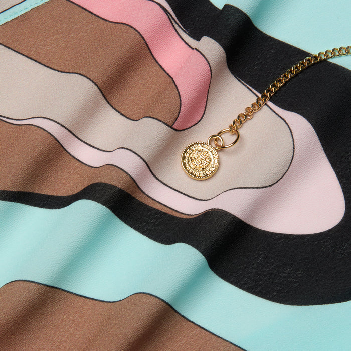 An Elise Cover-Up Dress in vibrant, abstract swirl print—featuring shades of blue, pink, brown, and black—serves as the backdrop for a gold coin pendant necklace.