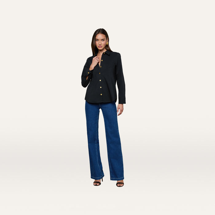 Wearing the Ellery Button-Down Shirt in black and a pair of blue jeans, a woman poses against a plain white background with one hand near her collar and the other resting by her side.