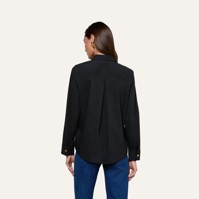 A woman with long brown hair is shown from the back against a plain light background, wearing the Ellery Button-Down Shirt in black stretch cotton and blue jeans.