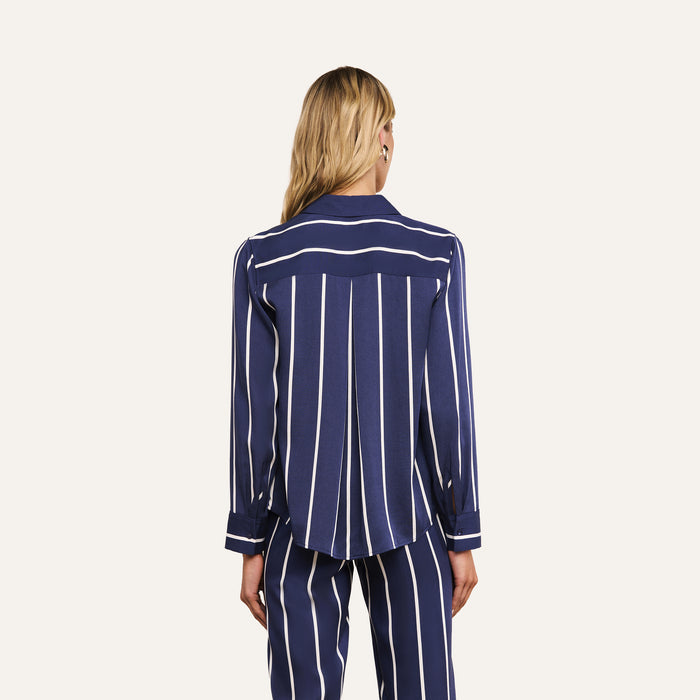 A person with long blonde hair is shown from the back against a plain white background, wearing the Ellery Shirt—a navy blue piece with white vertical stripes. The relaxed fit and lightweight tencel fabric offer effortless style and comfort.