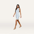 A woman with long brown hair walks confidently against a plain white background wearing the Ellis Tank Dress in pale blue and nude heels.