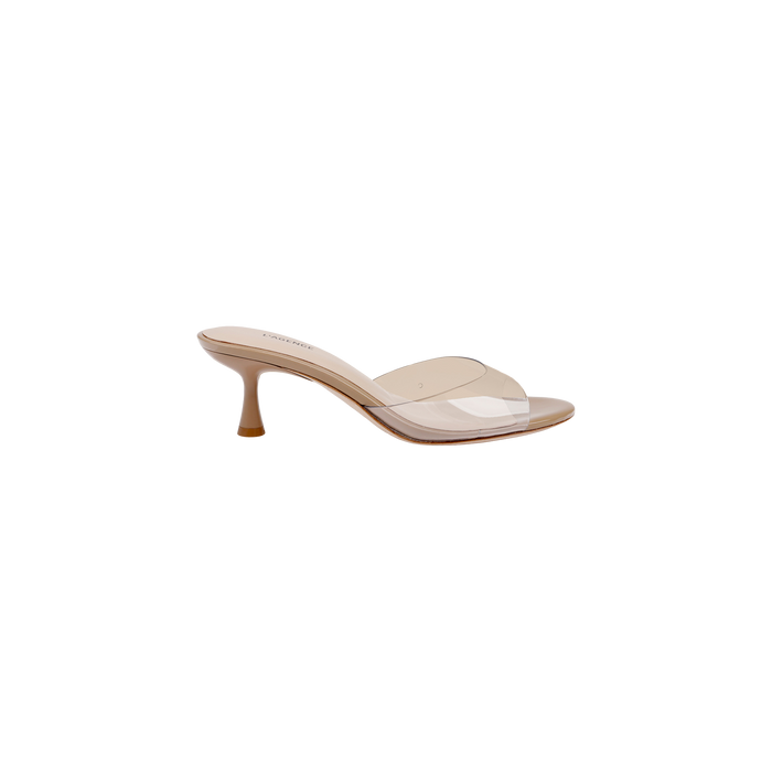 The Esther Kitten-Heel Mule features a nude color with a clear vinyl upper strap across the front, an open toe design, and a mid-height stiletto heel, displayed against a white background.