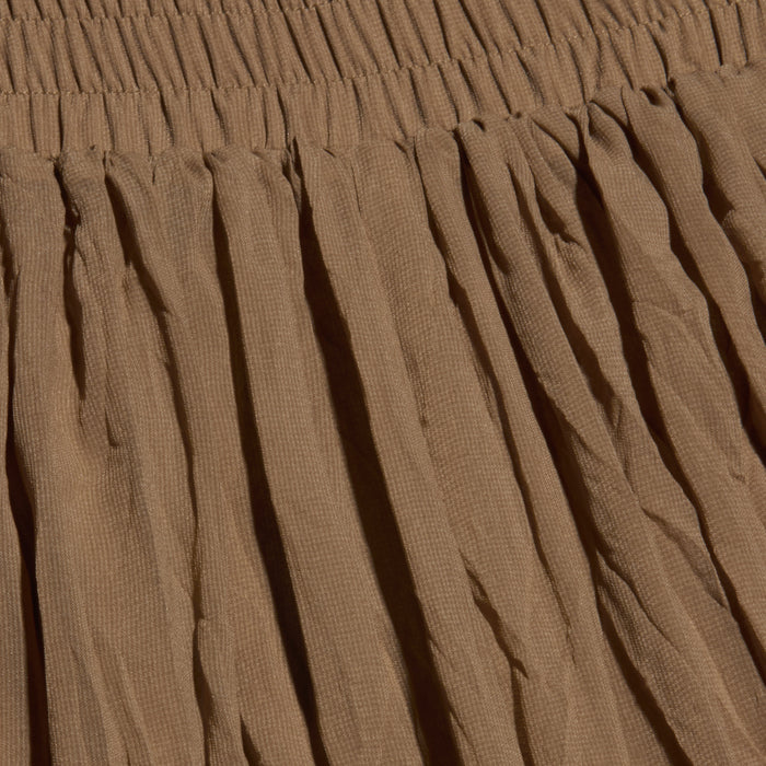 Close-up of the Ethel Pleated Pant in brown, featuring a gathered, elastic waistband at the top. The fabric displays vertical pleats and a subtly crinkled texture.