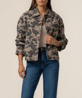 Woman wearing a taupe denim jacket with dark leopard print pattern and button front, styled over a cream top and blue jeans.