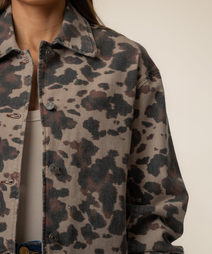 Taupe denim jacket with black leopard print pattern and button front closure worn over a ribbed cream top.