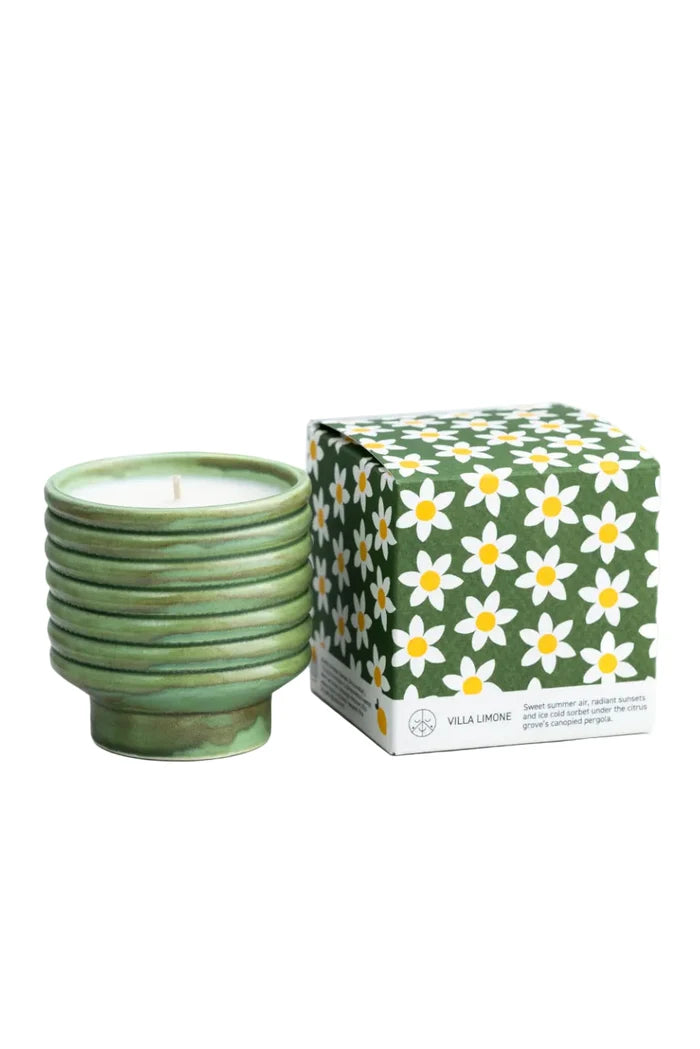 Candle in green ceramic vessel next to floral printed box on white background