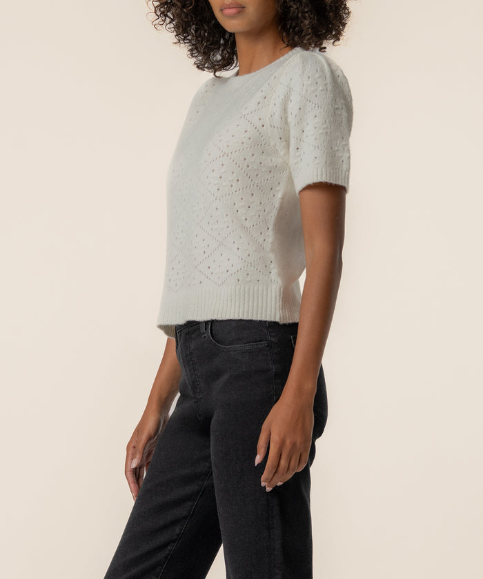 Cream short-sleeve sweater with textured knit pattern worn with black jeans.