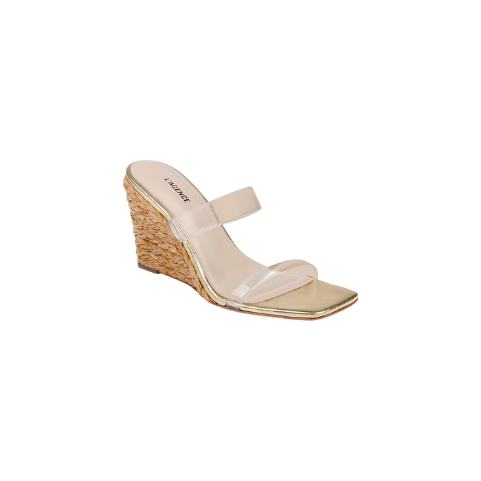 The Farrell Wedge Espadrille features a gold finish with a woven raffia wedge heel, square toe, and two clear straps across the top, displayed on a white background.