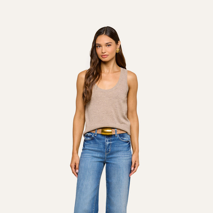 A woman stands facing forward, wearing the Filou Cashmere Tank in beige and blue jeans with a brown belt, against a plain light background.