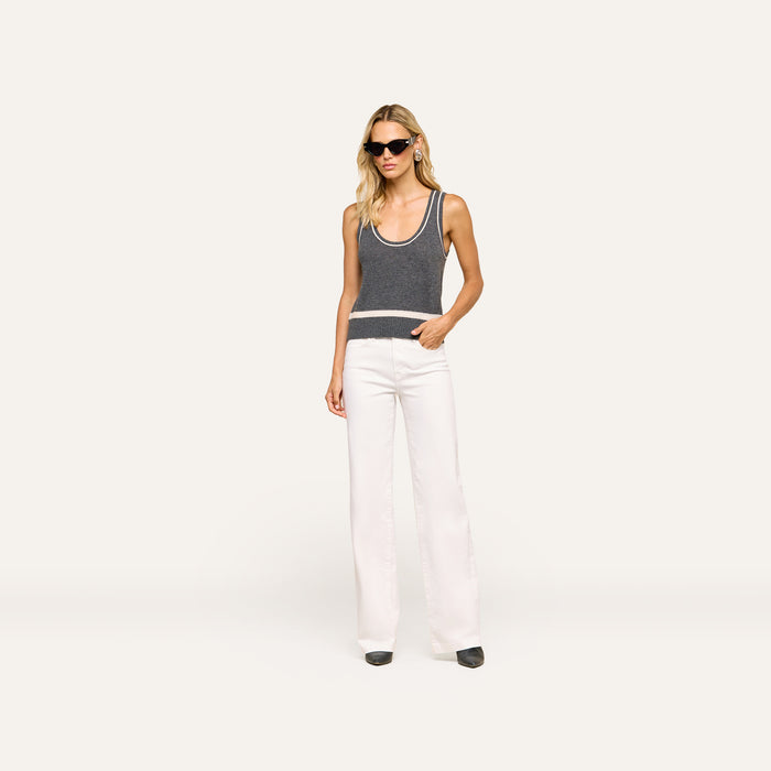 A woman stands confidently against a plain, light background with one hand in her pocket, wearing sunglasses, the Filou Cashmere Tank, white high-waisted wide-leg pants, and black shoes.