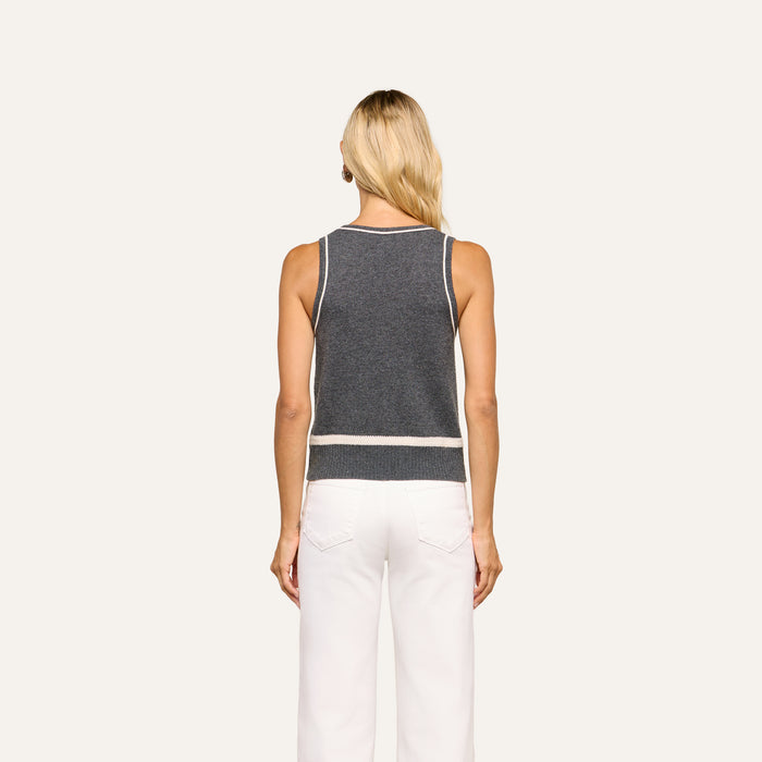 A woman with long blonde hair stands with her back to the camera, wearing the Filou Cashmere Tank in dark gray with white trim paired with white pants, set against a plain light background.