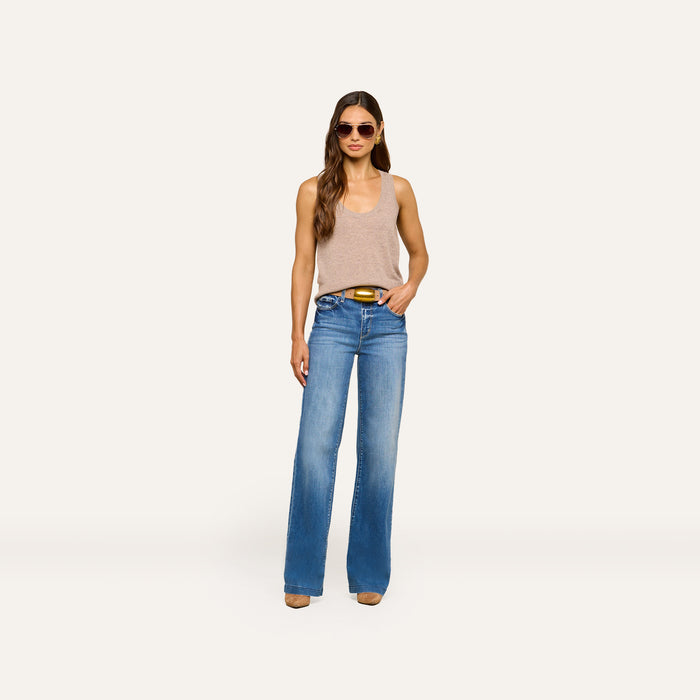 A woman wearing sunglasses, the Filou Cashmere Tank in beige, blue high-waisted wide-leg jeans, and brown shoes stands confidently with one hand in her pocket against a plain white background.