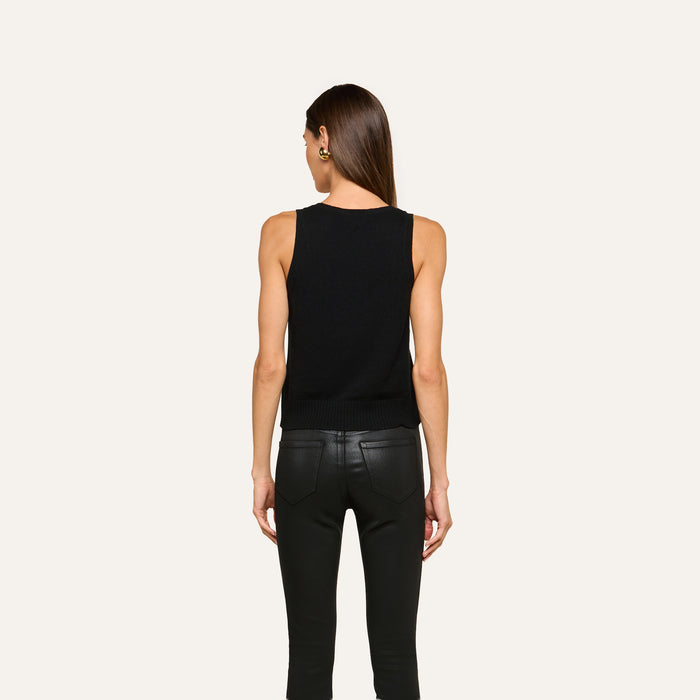 A woman with straight brown hair, wearing the Filou Cashmere Tank in black and black leather pants, stands facing away against a plain light background.