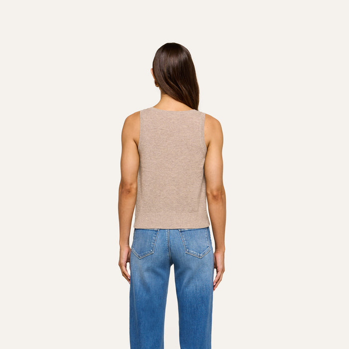 A person with long brown hair stands facing away, wearing the Filou Cashmere Tank in sleeveless beige and blue jeans against a plain light background.