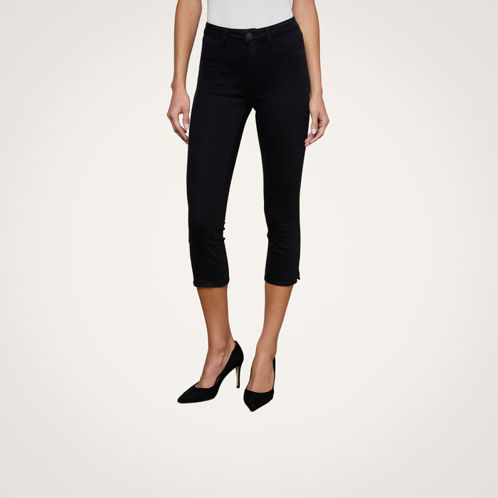 A person is shown from the waist down wearing the Fiora Pedal Pusher Jean in black super stretch denim, paired with a white top and black high heels, standing against a plain light background.