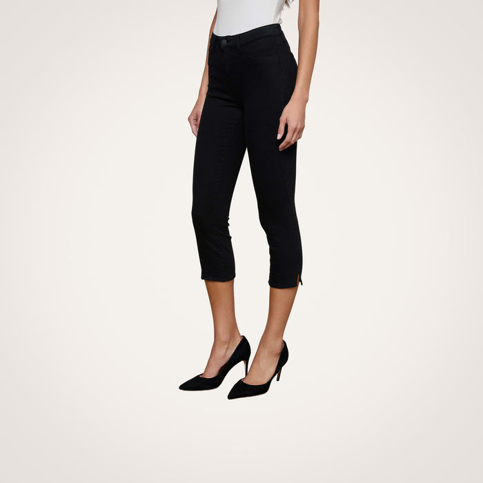 A woman models the Fiora Pedal Pusher Jean in black paired with black heels, standing against a plain white background. Only her lower body is shown, with her hands relaxed at her sides.