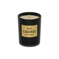 A black candle jar with a beige label displaying “Fleur D’Amour,” containing an unlit, cream-colored soy-blend wax candle infused with baccara rose.