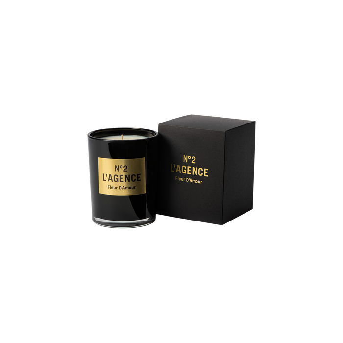 A black glass candle labeled Fleur D’Amour, crafted from soy-blend wax, is displayed beside a coordinating black and gold box on a white background.