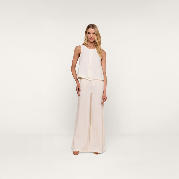 A woman stands against a plain white background wearing the Foster Linen Top, a sleeveless design with an A-line silhouette, paired with matching wide-leg pants and open-toe sandals.
