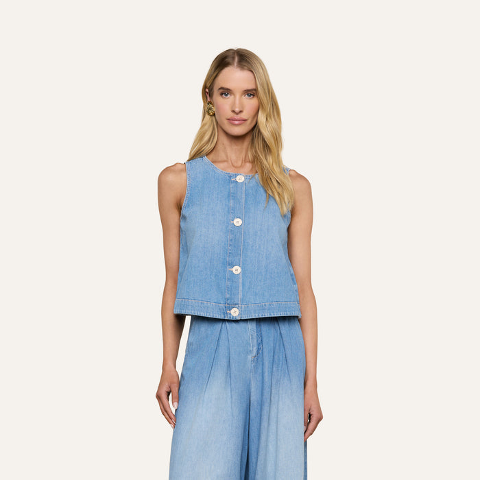 A woman stands against a plain, light background, wearing the Foster Top—a sleeveless piece crafted from featherweight denim—paired with matching wide-leg denim pants.