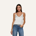 Model wearing the Gabriella Silk Camisole in ivory, paired with blue jeans, stands against a plain light background with one hand in her pocket and a relaxed expression.