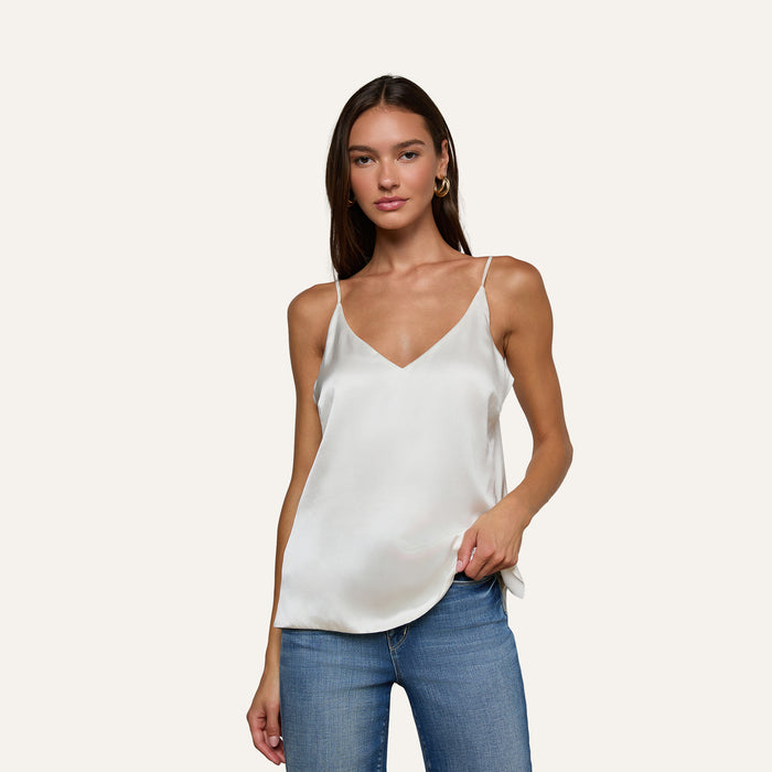 A woman wearing the Gabriella Silk Camisole in ivory and blue jeans stands against a plain light background, looking at the camera with a neutral expression.