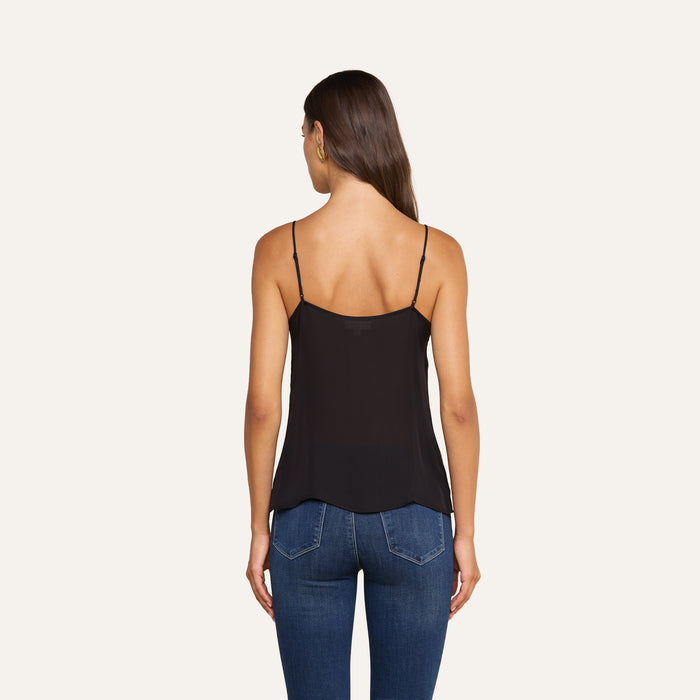 A woman faces away, wearing the Gabriella Silk Camisole in black and blue jeans, standing against a plain light background.