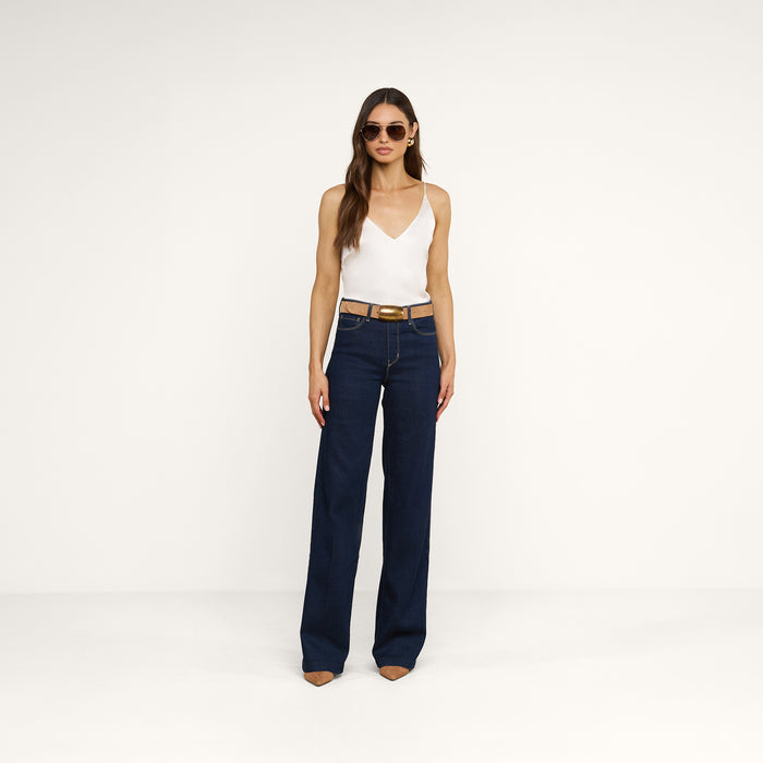 A woman wearing sunglasses, the Gabriella Silk Camisole in ivory, dark high-waisted wide-leg jeans, and brown pointed-toe shoes stands against a plain white background.