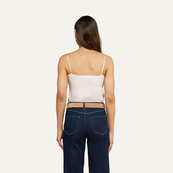 A woman with long brown hair, wearing the Gabriella Silk Camisole in ivory and blue high-waisted jeans, stands facing away against a plain light background.